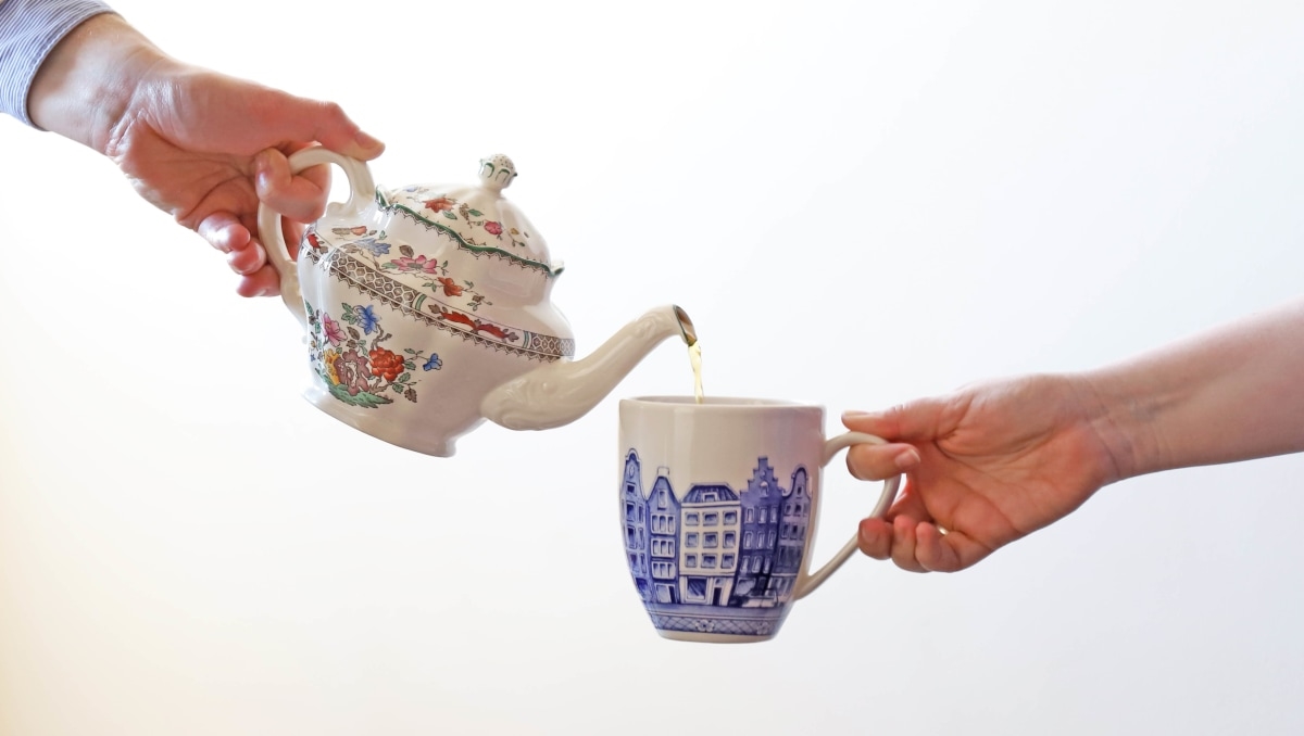 One hand pouring tea from teapot into a mug being held by someone else's hand