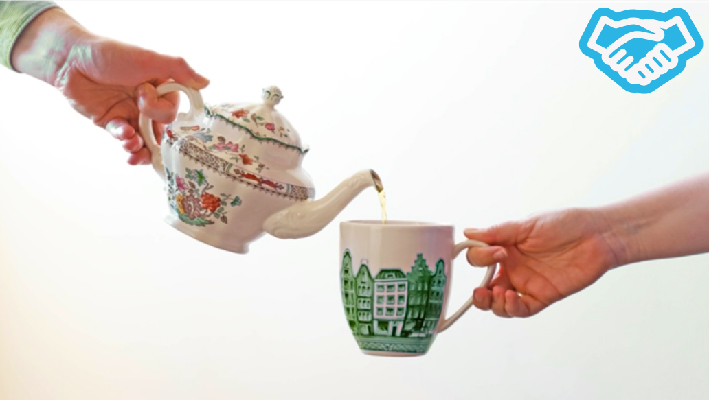 One hand pouring tea from teapot into a mug being held by someone else's hand
