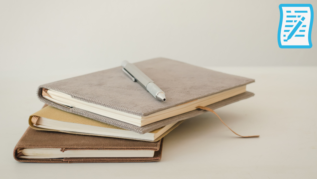 Three notebooks laid on top of each other, pink and brown ones are closed and the top one is open