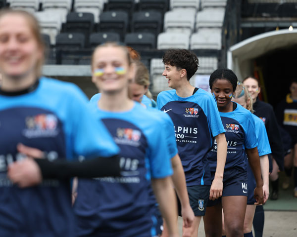 Guy's, King's & St Thomas' Women's Football Club members wearing their kit and smiling as they walk onto the pitch