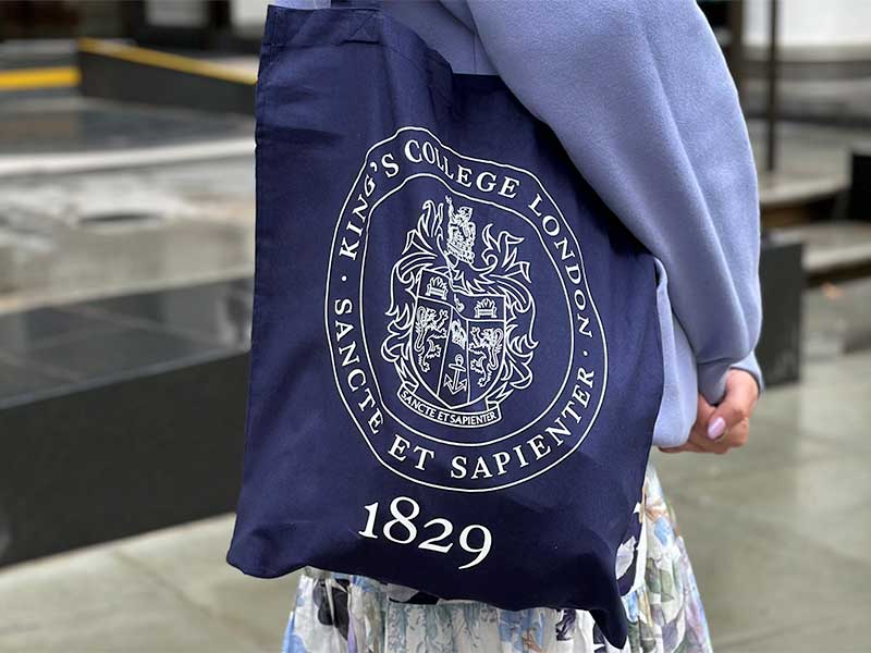 A blue tote bag with the KCL crest