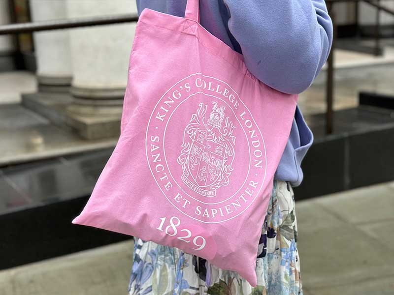 A pink tote bag with the KCL crest