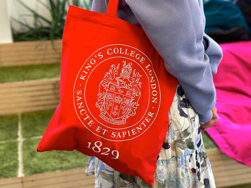 A red tote bag with the KCL crest