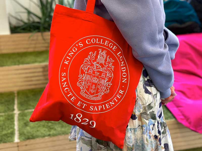 A red tote bag with the KCL crest