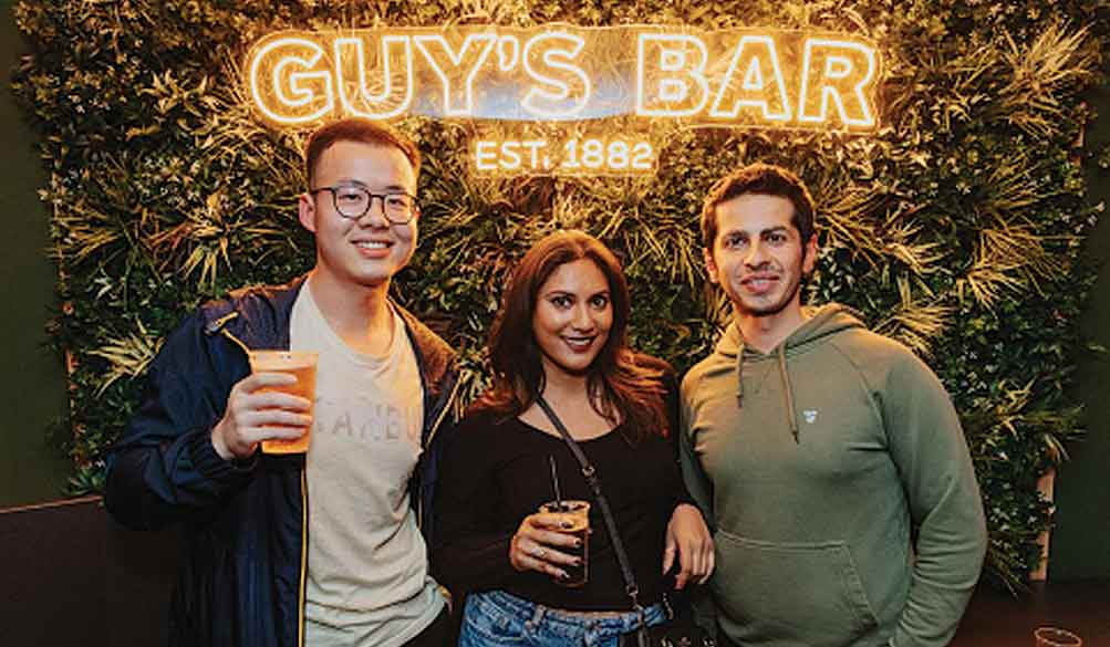 Students in Guy's bar holding drinks and smiling at the camera